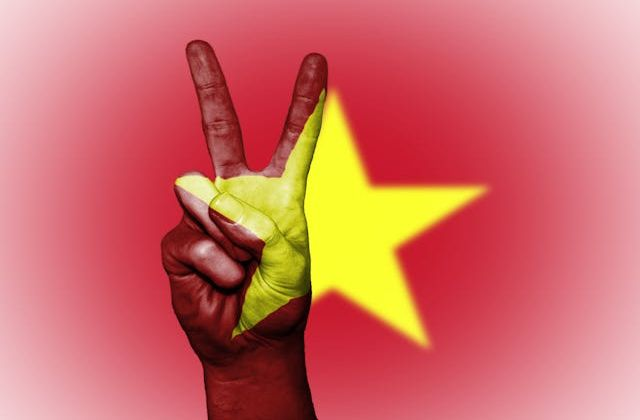 Hand showing peace sign in front of Vietnam national flag promoting affordable and culturally rich travel destinations