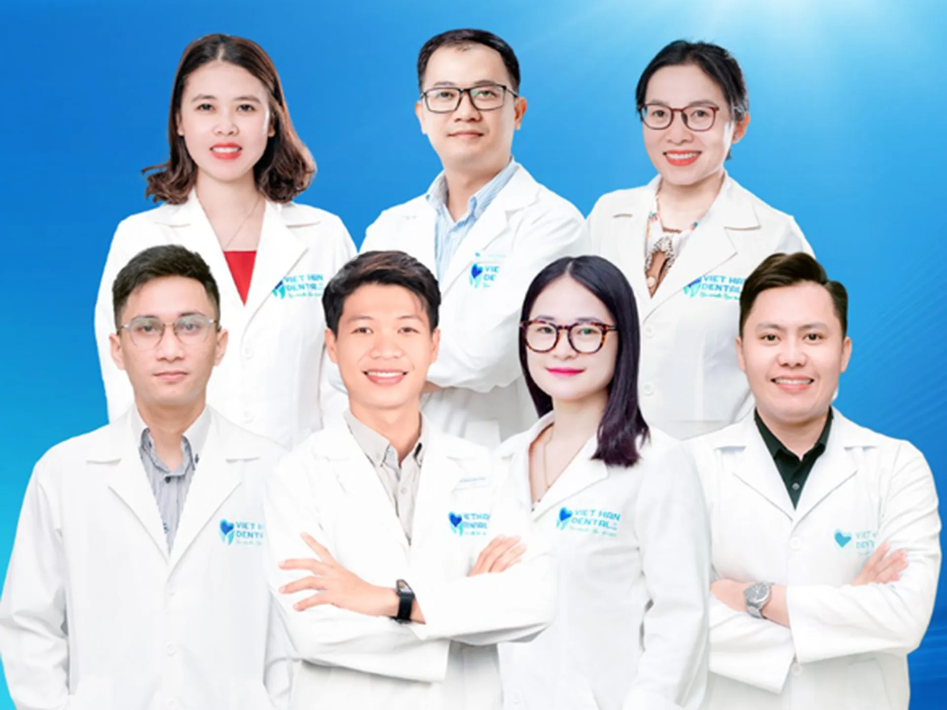 Professional dental team of Viet Han Dental Clinic in Nha Trang posing in lab coats against blue background