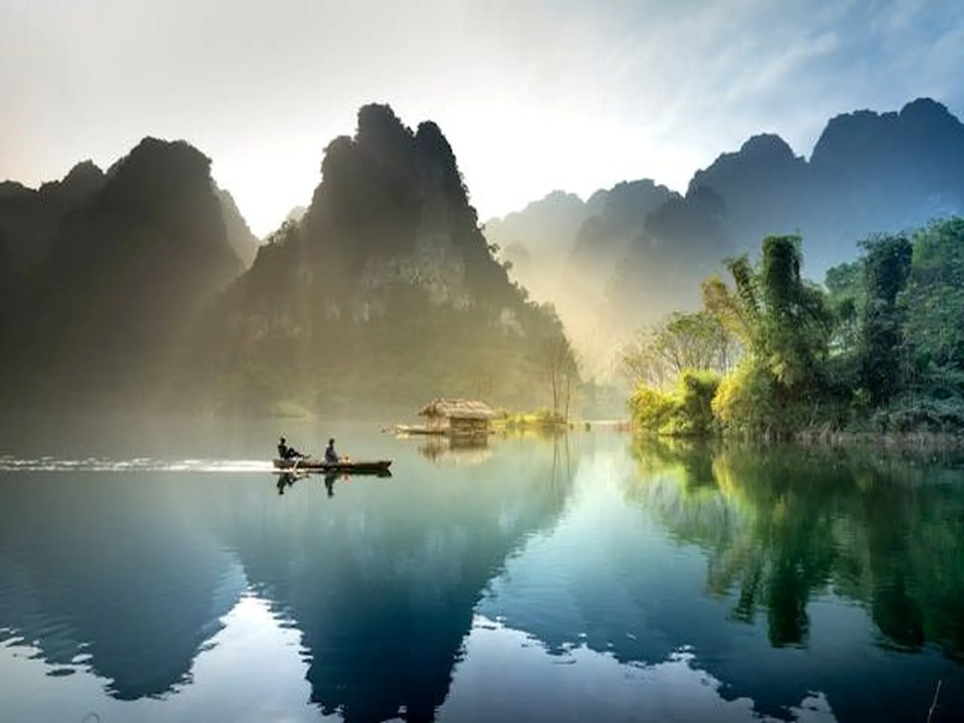 Image of a boat on a lake in Vietnam with a background of pointy mountains, a kind of scenery you would see in regional Vietnam